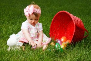 Baby playing with Easter eggs while sitting beside a spilled red basket
